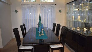 A dining room with a glass table, black chairs, a teal table runner, a Christmas tree, and a glass display cabinet. - 3bed/2bath pool home, sleeps 8 guests, great location, private/sunny aspect. (Davenport)
