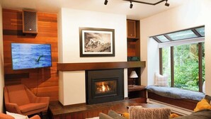 A living room with a fireplace, a television, and a window with a view of greenery.