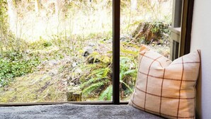A window with a view of a forested area, a cushion, and a window frame.