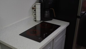 Cozinha compacta com bancada branca, fogão por indução preto, cafeteira e geladeira.
