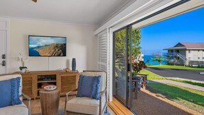 Uma sala de estar com uma janela grande, um sofá, uma mesa de centro de madeira e uma televisão na parede.
