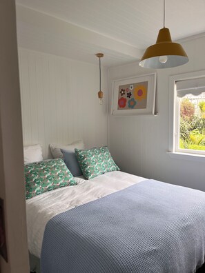 A bedroom with a bed, pillows, a hanging light fixture, a window, and a wall-mounted picture.