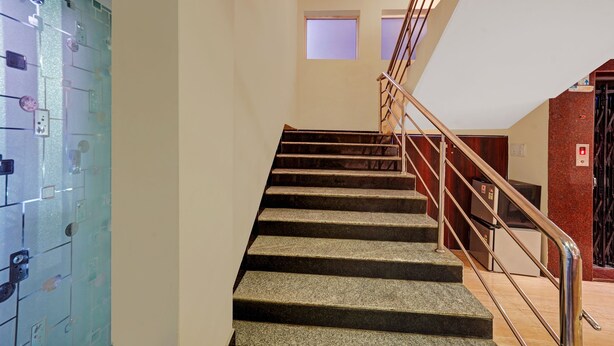 A staircase with metal railings, a light-colored wall, and a door with a lock on the left. - Treebo Savera Grand (Vijayawada)