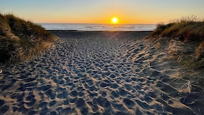 Ein Sandweg am Strand, der zum Meer führt, mit untergehender Sonne im Hintergrund.