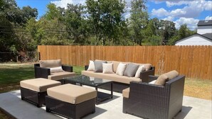 An outdoor patio with a sectional sofa, two ottomans, and a glass coffee table.