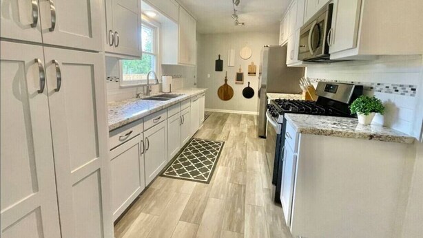 A modern kitchen with white cabinetry, a central island, a microwave, and a stove.