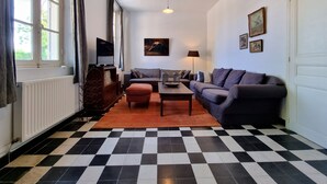 Una sala de estar con piso a cuadros, un sofá gris, una mesa de centro de madera y un televisor sobre un mueble de madera.