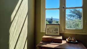 Una habitación con ventana, una mesa con un cuadro enmarcado y una caja pequeña, y un plato con dos pasteles.