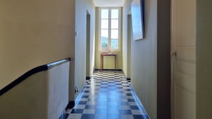 Un pasillo con piso de cuadros, una ventana al final y una puerta a la derecha.