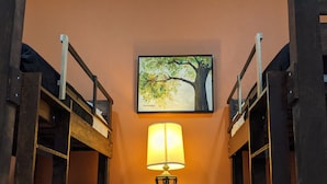 Un pasillo con una escalera de madera, una lámpara de pared y un cuadro enmarcado con un árbol.