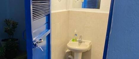 A small bathroom with a white sink, a window, and a blue door.