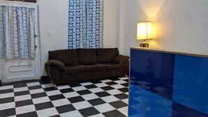 Una habitación con piso a cuadros, un sofá marrón, una puerta con cortinas y una lámpara fijada a la pared.
