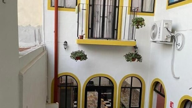 Un pequeño comedor con una mesa y sillas de madera, una ventana con marco amarillo y una planta en maceta en el alféizar.