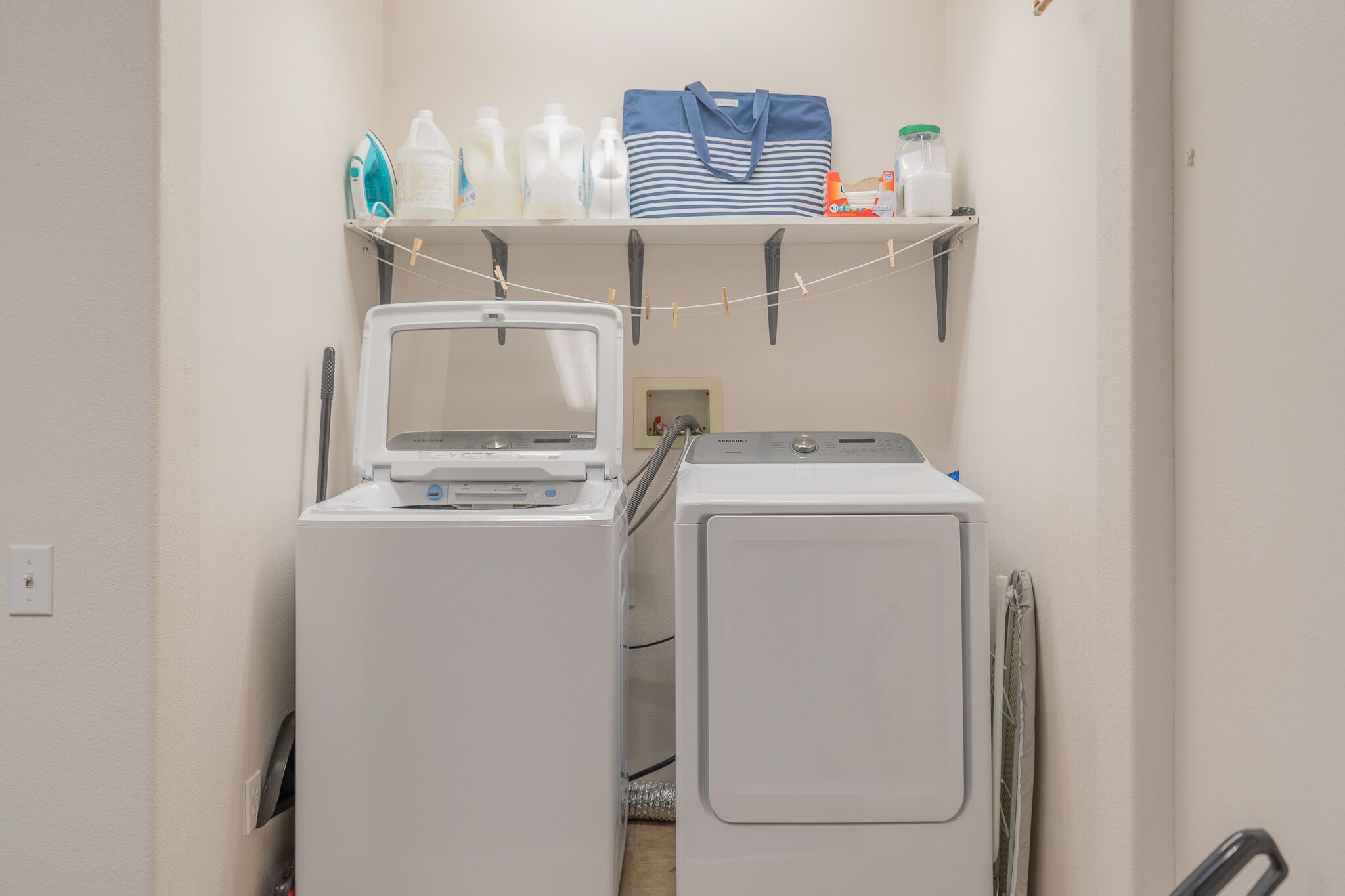 A laundry area with two washing machines and a shelf above containing bottles and a bag.