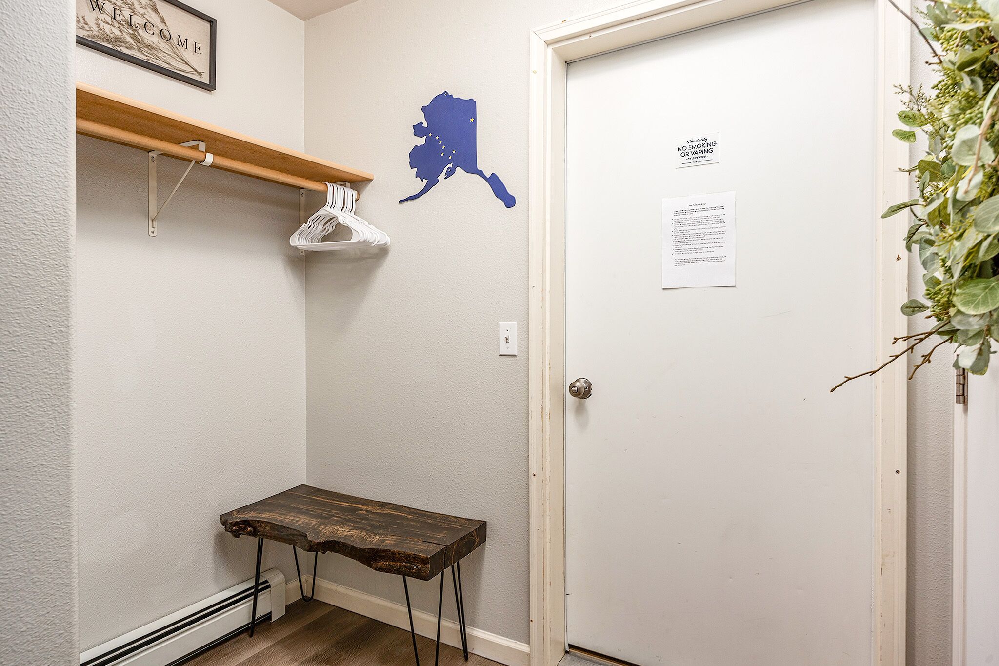 Un couloir avec un porte-manteau, une table en bois, une porte sur laquelle est affichée une annonce et une carte de l’Alaska accrochée au mur.