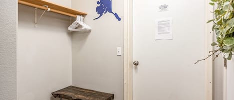 Un couloir avec un porte-manteau, une table en bois, une porte sur laquelle est affichée une annonce et une carte de l’Alaska accrochée au mur.