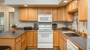 A kitchen with wooden cabinets, a white stove, a microwave, and a sink. - Borealis Abode: Abundant Amenities; Private Hot Tub, Pool Table, and King Bed (North Pole)