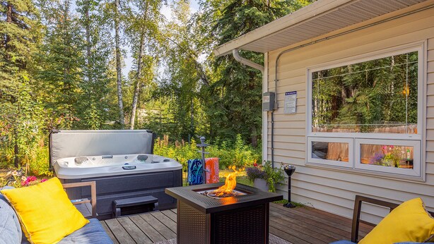 A cozy outdoor seating area with a fire feature, a hot tub, and a view of a forested area. - Borealis Abode: Abundant Amenities; Private Hot Tub, Pool Table, and King Bed (North Pole)