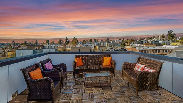 Terraza en la azotea con mobiliario de mimbre y vistas a un paisaje urbano al atardecer.
