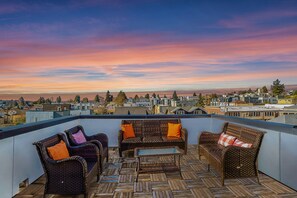 A rooftop terrace with wicker furniture and a view of a cityscape during sunset. - Luxe home near Space Needle & Lumen Field w/Views (Seattle)