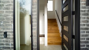 Un interior moderno con pared de ladrillo, escalera de madera y puerta negra con paneles de vidrio.