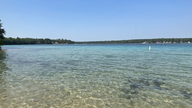 Una vista nítida d'una platja amb aigües tranquil·les i una riba llunyana.