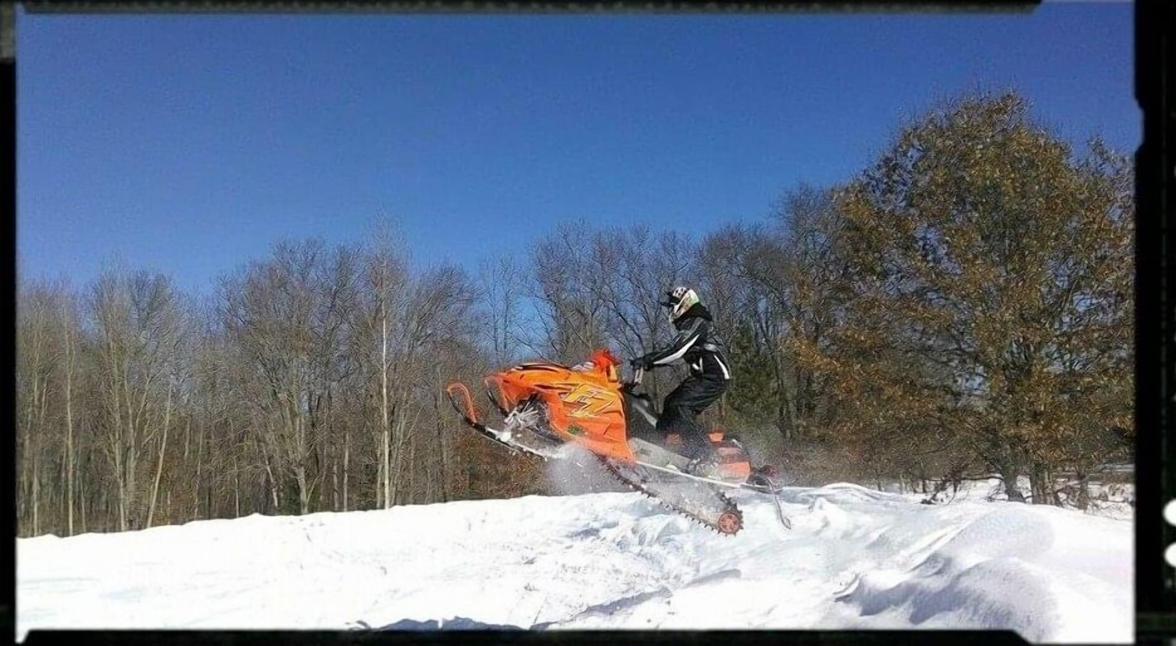 Eine Person fährt mit einem orangenen Schneemobil Ski.