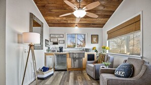 A compact kitchen with a wooden ceiling, a dining area with a sofa, and a window with blinds. - Honeysuckle Beach House - Next to Shady Gators - Private Beach! (Lake Ozark)