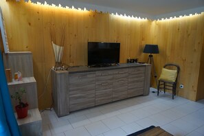 Ett modernt vardagsrum med ett träskåp, en platt-TV, en lampa och en stol.