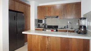 A kitchen with wooden cabinets, a refrigerator, a microwave, a stove, and a blender. - Confidence Luxurious Apartment (Santiago de los Caballeros)