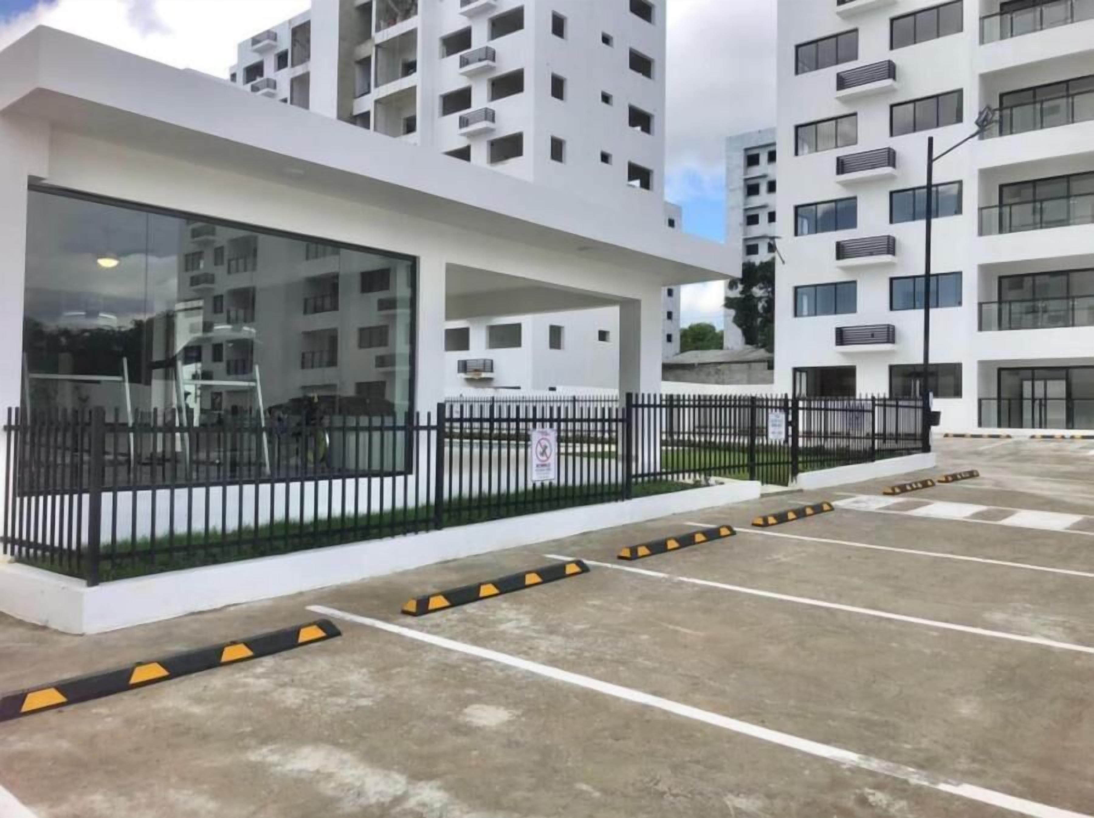 A modern building with a white facade, large windows, and a black fence.