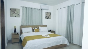 A bedroom with a bed, a nightstand, a lamp, and two wall-mounted air conditioners. - Confidence Luxurious Apartment (Santiago de los Caballeros)