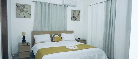 A bedroom with a bed, a nightstand, a lamp, and two wall-mounted air conditioners.
