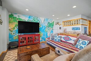 Ein Wohnzimmer mit einem großen Flachbildfernseher, einem roten Schrank, einem gemusterten Sofa und einer Wandkarte.