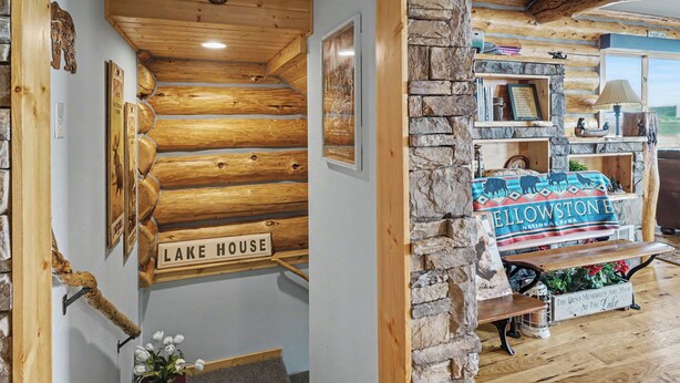 Ein gemütliches Interieur mit einer Holzwand mit Protokollen, auf der 'LAKE HOUSE' steht, einem Steinkamin und einer Bank mit einem Schild, das 'YELLOWSTONE NATIONAL PARK' zeigt.