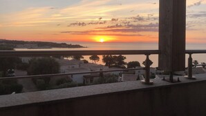A sunset view from a balcony overlooking a coastal area with buildings and trees. - Mini Villa avec imprenable vue sur la mer (Lumio)