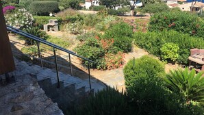 A garden with a stone staircase leading to a balcony overlooking a coastal area with houses and a beach. - Mini Villa avec imprenable vue sur la mer (Lumio)