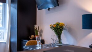 A hotel room with a TV mounted on the wall, a table with a vase of flowers, and a chair. - Talisker Apartment in Oban Town Centre (Argyll and Bute Council)