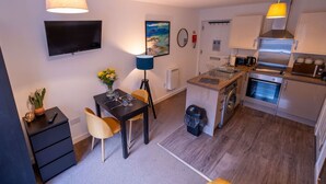 A compact kitchen with a dining area, a washing machine, and a TV mounted on the wall. - Talisker Apartment in Oban Town Centre (Argyll and Bute Council)
