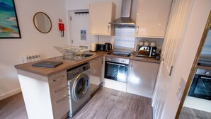 A compact kitchen with a washing machine, oven, microwave, and a coffee maker. - Talisker Apartment in Oban Town Centre (Argyll and Bute Council)