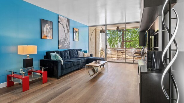 Uma sala de estar moderna com uma parede azul, um sofá preto, uma mesa de centro de vidro e uma mesa lateral vermelha.