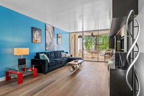 Ein modernes Wohnzimmer mit blauer Akzentwand, einem schwarzen Sofa, einem Glastisch und einem roten Beistelltisch.