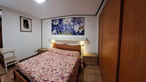 Un dormitorio con cama, mesitas de noche, un armario y un cuadro de flores en la pared.