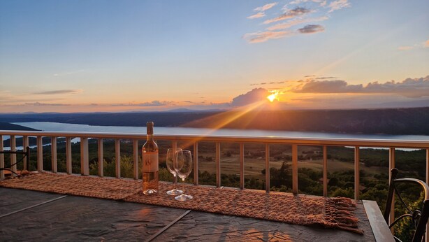 Una mesa con una botella y vasos, con vistas a un paisaje pintoresco al atardecer.