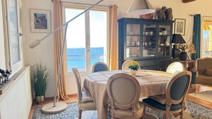 Un comedor con una mesa, sillas, un armario y vista al mar.