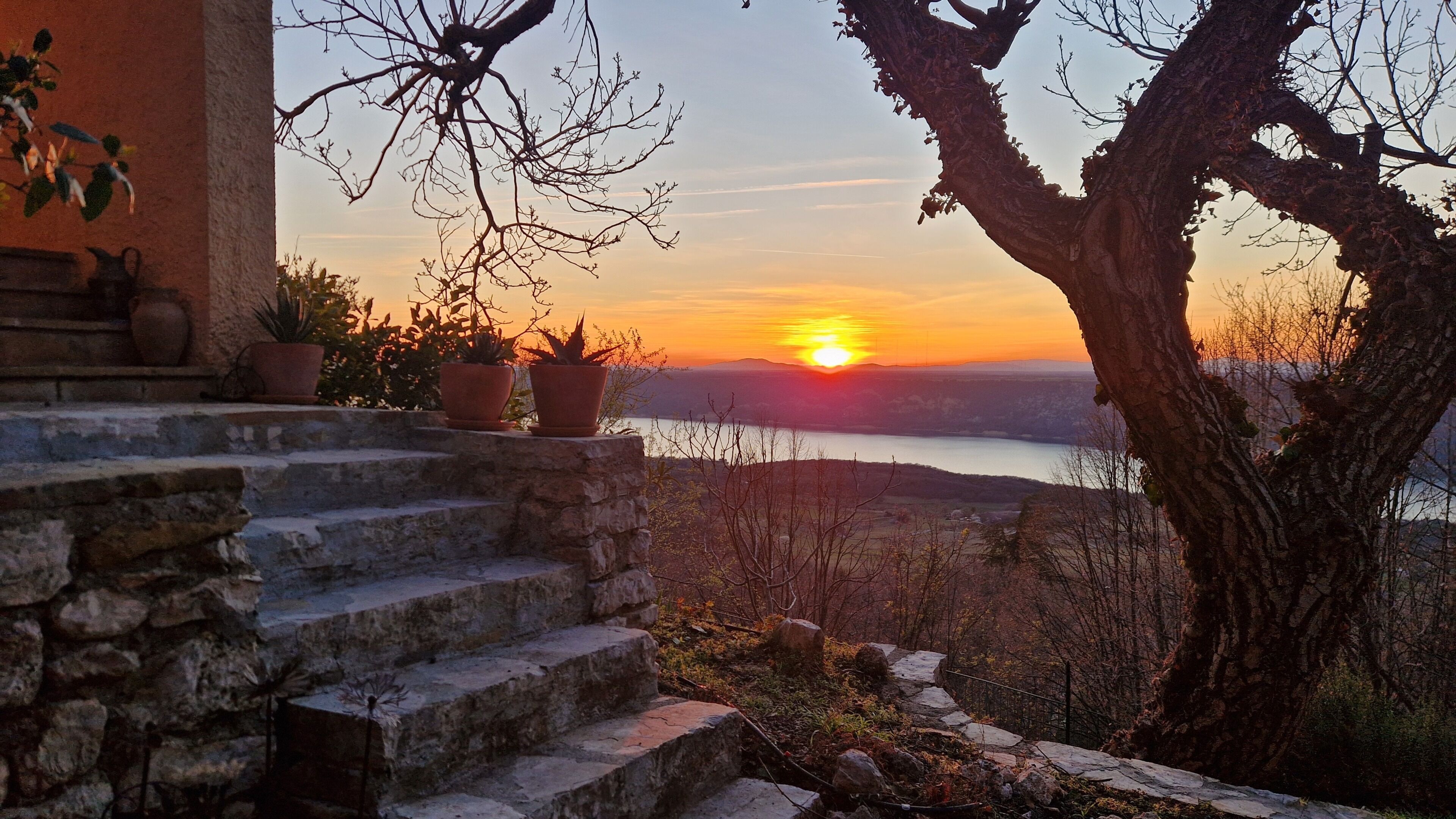 A stone staircase leading to a terrace overlooking a sunset over a body of water.