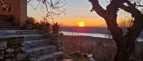 A stone staircase leading to a terrace overlooking a sunset over a body of water.