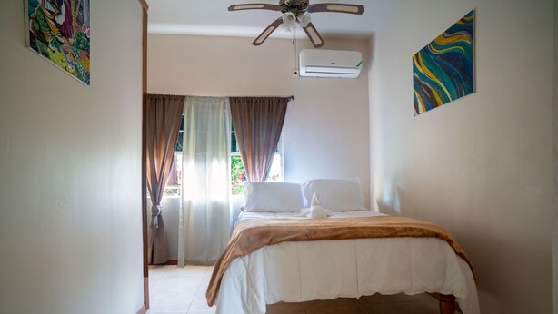 A bedroom with a bed, a ceiling fan, an air conditioner, and a view of the outdoors. - Eleven30 Luxury Apartments  (Negril)