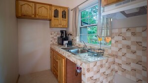 A kitchen with wooden cabinets, a window with a view, a sink, and a tiled backsplash. - Eleven30 Luxury Apartments  (Negril)