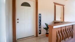 A reception area with a white door, a welcome sign, a potted plant, and a decorative wall feature. - Eleven30 Luxury Apartments  (Negril)